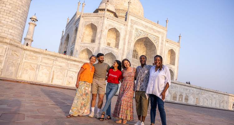 Des voyageurs souriants posent bras dessus, bras dessous devant le majestueux Taj Mahal en marbre blanc à l'aube.