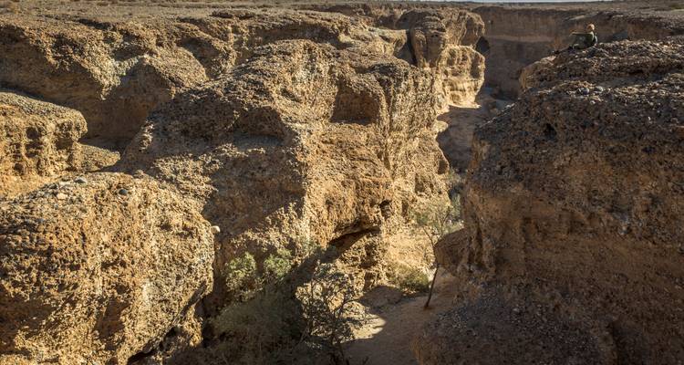 Des parois de canyon en grès escarpées avec un visiteur solitaire assis en hauteur au-dessus du ravin.