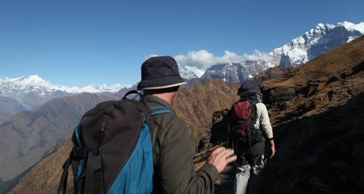 Les routards suivent un sentier de montagne escarpé avec des pics enneigés lointains au Népal.