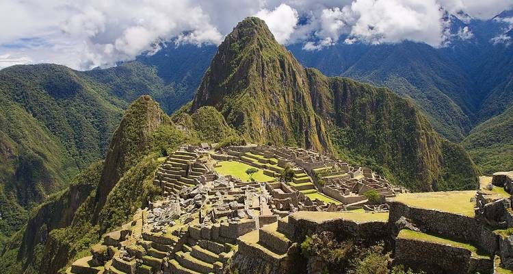 Panoramablick auf Machu Picchu mit terrassierten Hügeln und Bergen im Hintergrund.