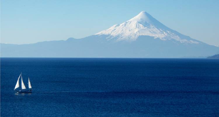 Le volcan Osorno aux pics enneigés s'élève au-dessus d'un immense lac bleu profond avec un voilier solitaire.