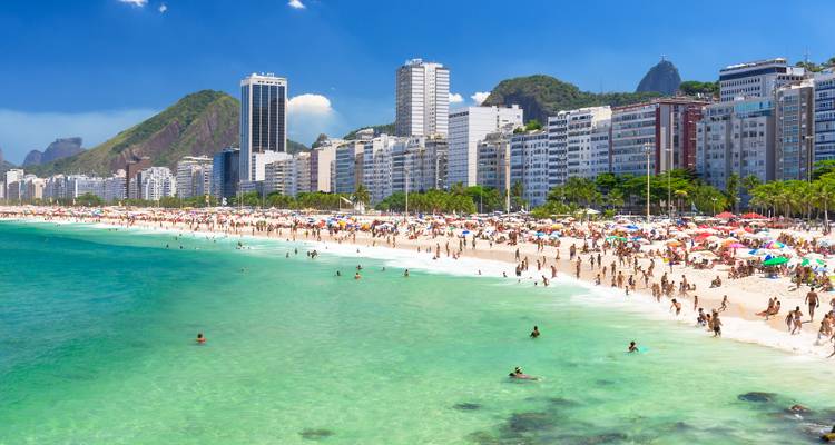 Plage de Copacabana bondée avec eau turquoise, hôtels de grande hauteur et collines verdoyantes se profilant à l'arrière-plan.