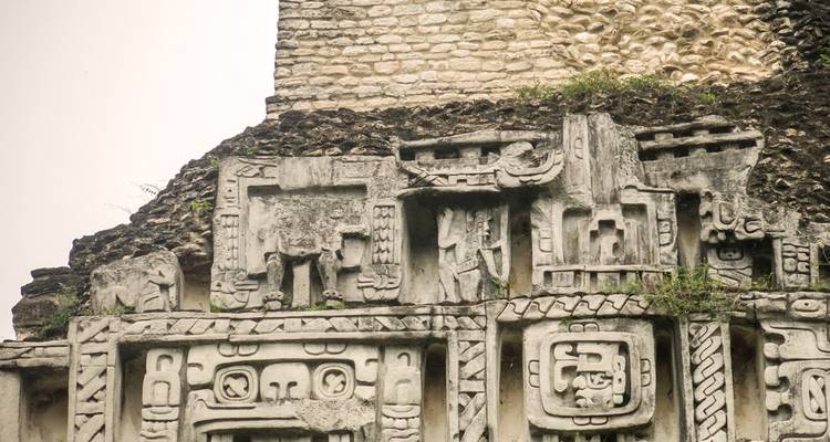 Friso de estuco detallado con glifos mayas antiguos y figuras en la fachada de una pirámide de piedra.