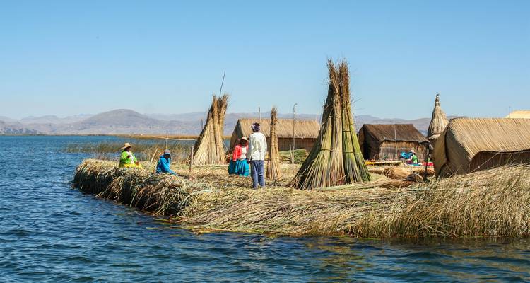 Les huttes de roseaux et les piles coniques flottent sur les eaux bleues des îles Uros du lac Titicaca avec des habitants au travail.
