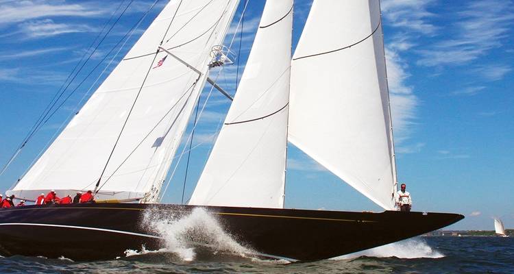 Sailboat with multiple sails on the water under a clear sky.