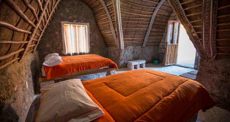Acogedora habitación rústica con dos camas cubiertas de naranja dentro de una cabaña de piedra con arco.