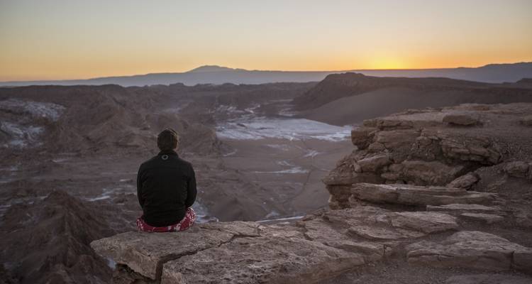 Person, die bei Sonnenuntergang auf einem Felsen in der Nähe einer Schlucht sitzt.