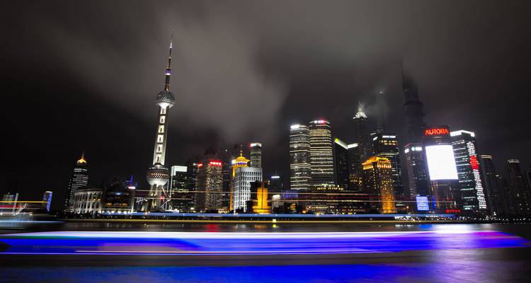 Panorama nocturna del horizonte iluminado de Shanghai con rastros de luz de un bote que pasa por el río