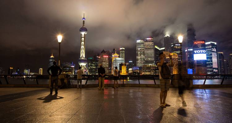 Visitantes en el Bund mirando hacia el otro lado del río hacia el brillante skyline de Shanghai bajo dramáticas nubes nocturnas
