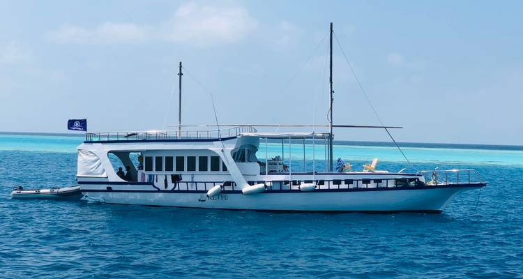 Navire de croisière avec hébergement à bord ancré sur une eau turquoise éclatante avec un récif visible en dessous.