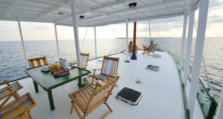 Zonnig jachtdek ingericht met fruit en houten stoelen met uitzicht over de rustige zee.