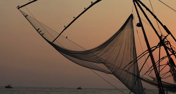 Silueta de redes de pesca chinas contra un cielo naranja al atardecer sobre el Mar Arábigo