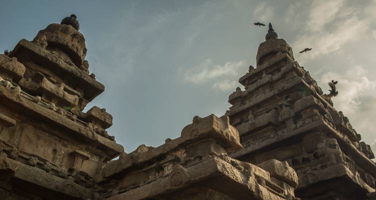 Las antiguas torres de piedra del Templo de la Orilla se alzan mientras los pájaros vuelan en círculos bajo un cielo sombrío