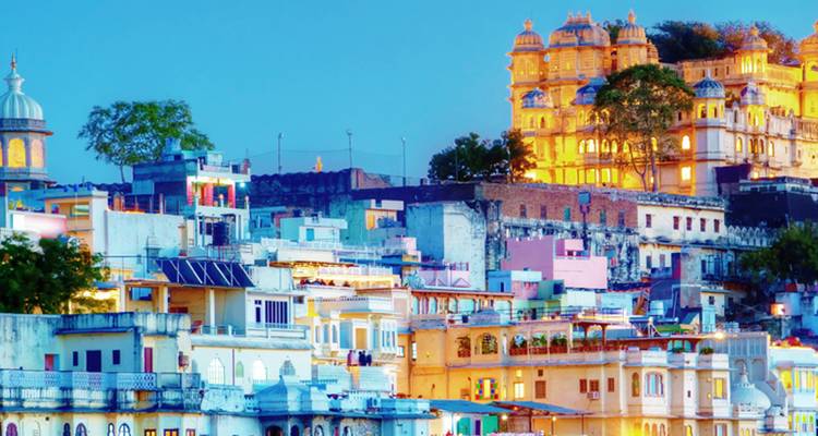 Colourful houses cluster below a hilltop palace glowing at twilight in Udaipur.