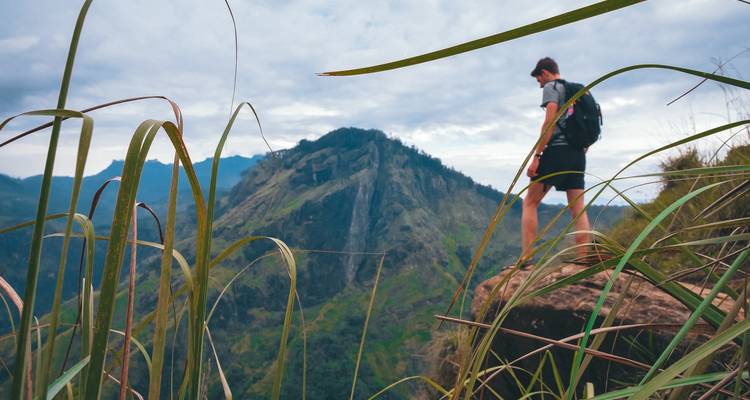 Een wandelaar die op een rots staat en uitkijkt over een berglandschap.