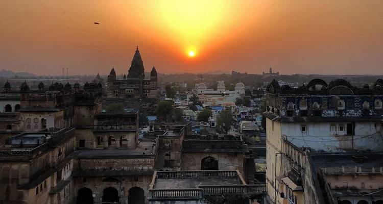 Le soleil orange se couchant derrière les temples historiques et les toits de la ville d'Orchha.