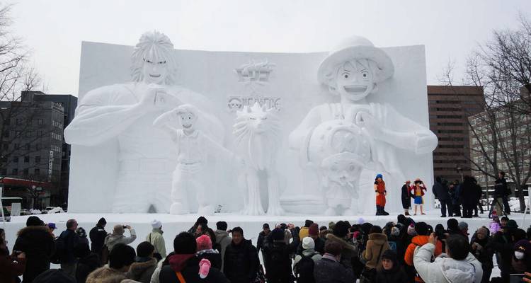 Une grande sculpture de neige représentant des personnages d'anime s'élève au-dessus d'une foule lors d'un festival d'hiver.