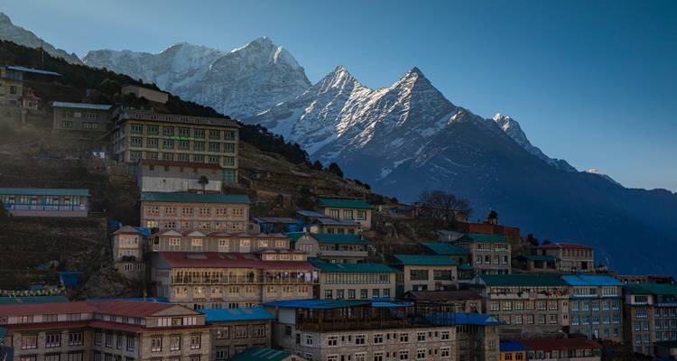Pueblo de montaña en terrazas de Namche Bazaar con picos blancos imaculados elevándose detrás