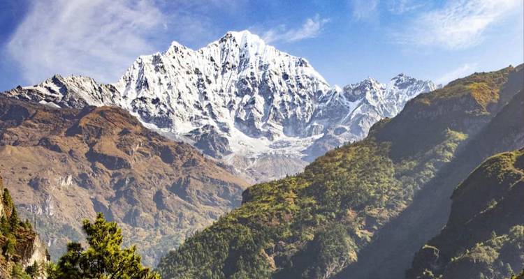 Un majestuoso pico nevado del Himalaya domina un cielo azul despejado sobre colinas rocosas