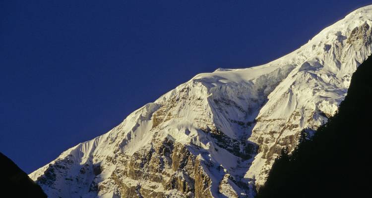 Cresta de nieve afilada de un pico del Himalaya recortándose contra el profundo cielo azul de la mañana