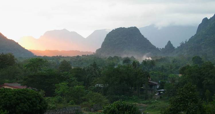 Lever de soleil brumeux sur une vallée tropicale luxuriante et des pics calcaires.