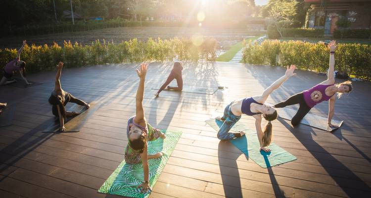 Les voyageurs s'étirent lors d'une séance de yoga en plein air sur une plateforme en bois au lever du soleil avec un effet de halo lumineux.