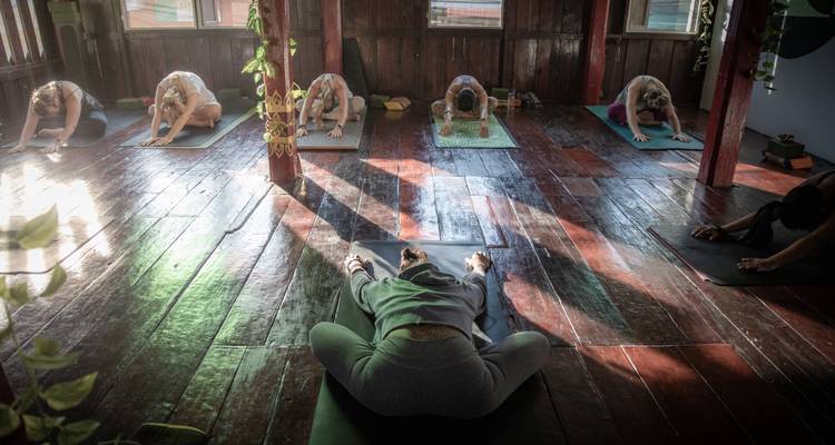 Les participants se détendent en posture de l'enfant lors d'un cours de yoga intérieur serein avec une lumière patterned sur des planchers en bois.