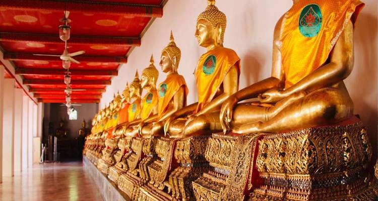 Fila de estatuas de Buda doradas sentadas envueltas en túnicas naranjas dentro de un pasillo del templo.