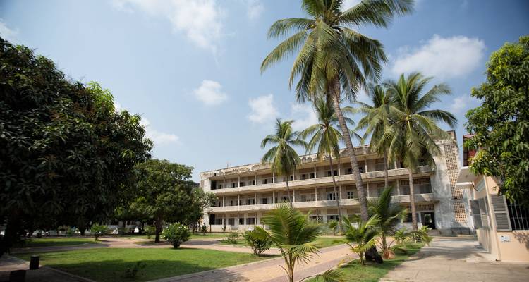 Extérieur des bâtiments du Musée du Génocide de Tuol Sleng encadrés par des palmiers et des pelouses