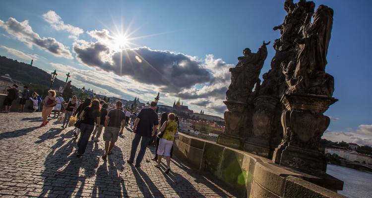 Las multitudes pasean por el icónico Puente de Carlos de Praga bajo un brillante sol de la tarde con estatuas esculpidas en silueta.