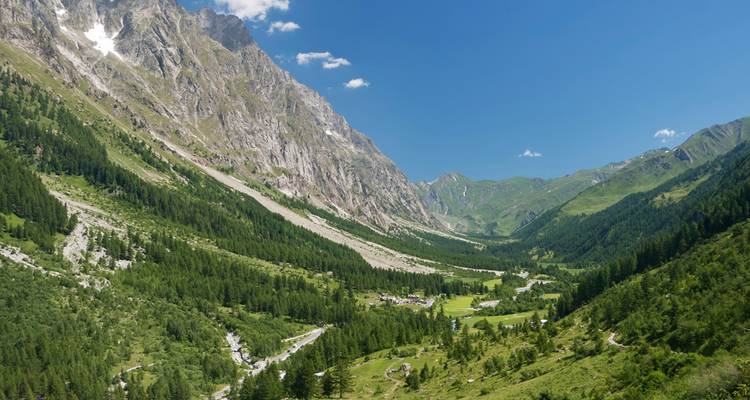 Vallée verdoyante avec une rivière sinueuse située sous des falaises alpines imposantes lors d'une journée d'été.