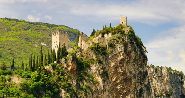 Les ruines d'un château de pierre médiéval perchées de manière spectaculaire au sommet d'une falaise rocheuse abrupte entourée de verdure.