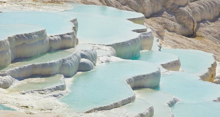 Türkisfarbene Mineralbecken, die über weiße Travertinterrassen hinab fließen.