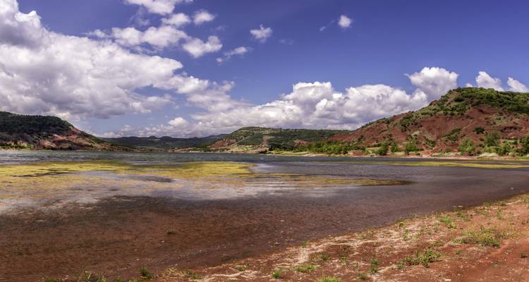 Vue panoramique d'un lac avec des collines ondulantes et des nuages.