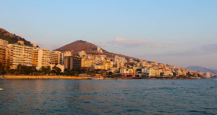 De kuststad Saranda strekt zich uit langs de baai tijdens het gouden uur met heuvels op de achtergrond.