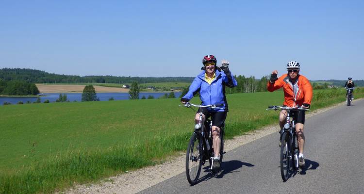 Ciclistas en una carretera rural con una vista panorámica de campos y un lago.