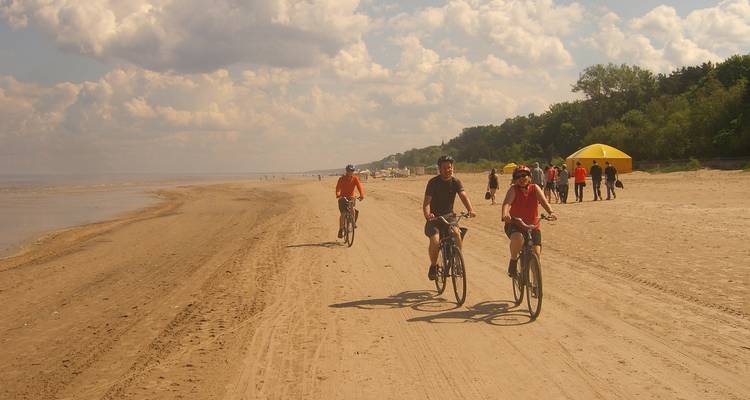 Gente pedaleando en una playa de arena con una tienda amarilla y un bosque al fondo.