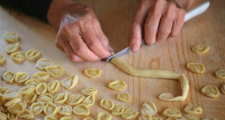 Des mains fabriquent des pâtes traditionnelles sur une surface en bois.