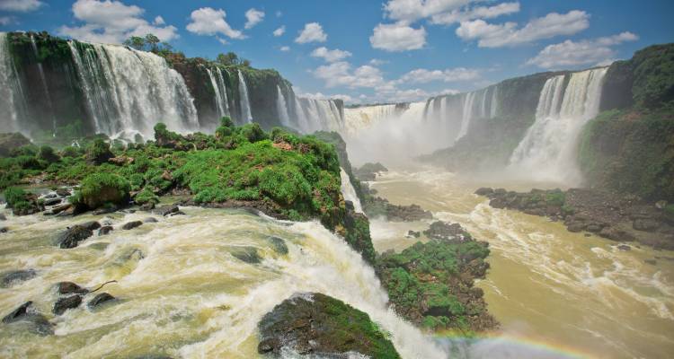 Vue panoramique des chutes d'Iguazu avec un arc-en-ciel et une végétation luxuriante.