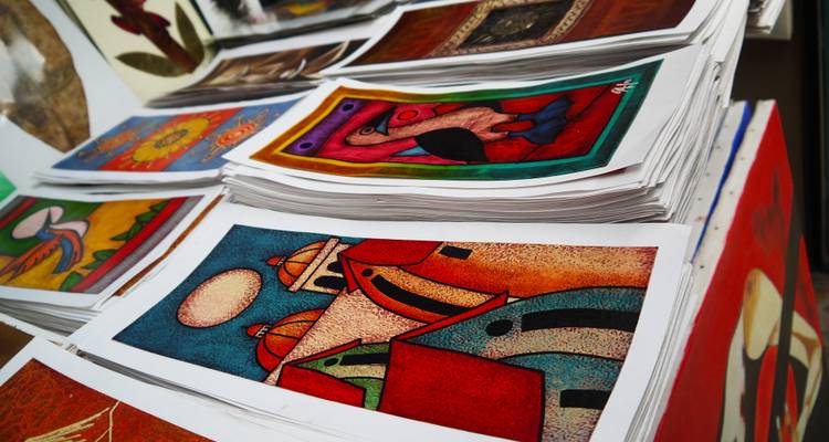 Colorful artistic prints stacked in an outdoor market.