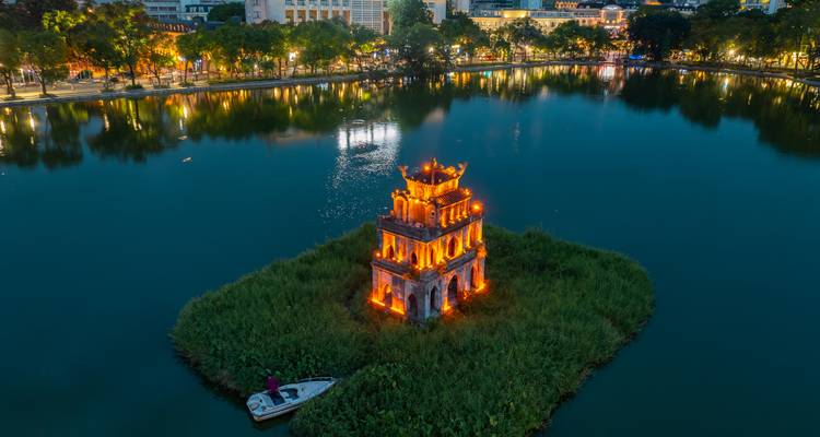 Torre iluminada en una isla exuberante dentro de un lago por la noche.