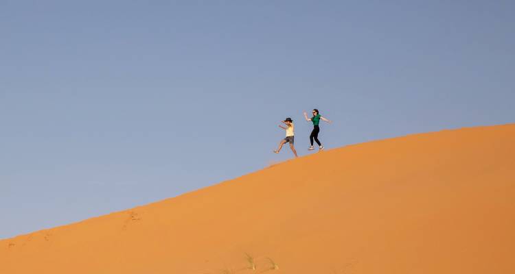Two people running down a sand dune in the desert.