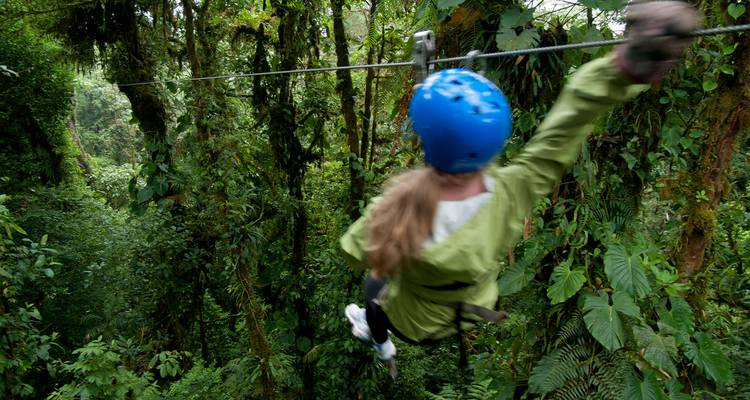Bewegungsunschärfe eines Zip-Liner in blauem Helm, der mit hoher Geschwindigkeit durch das dichte grüne Kronendach eines Nebelwaldes rast.