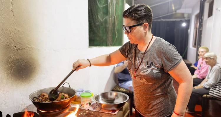 Person cooking in a kitchen with others in the background.