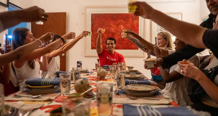 Cena donde los viajeros alzan las copas en un brindis alrededor de una colorida mesa mexicana.
