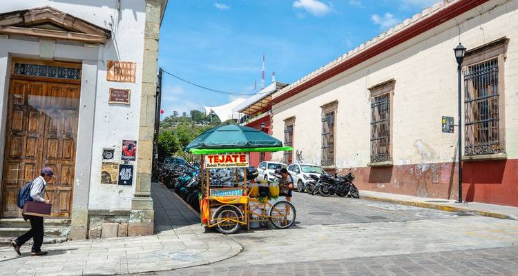 Esquina tranquila de calle colonial en Oaxaca con un colorido carrito de comida callejera etiquetado Tejate.