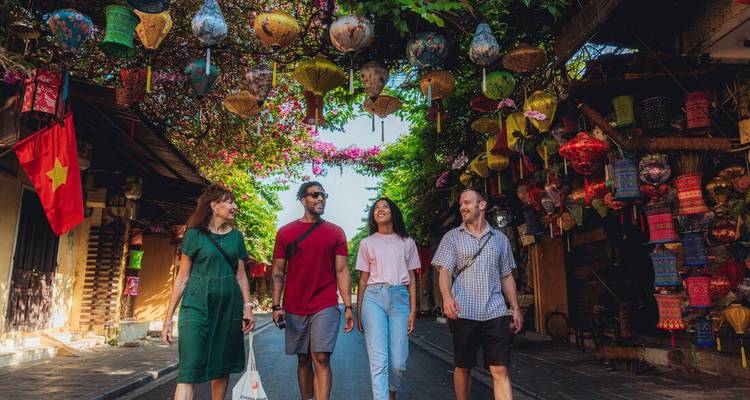 Vier reizigers flaneren onder een booggang van hangende lampionnen en bloemen op een charmante straatje in de oude stad.