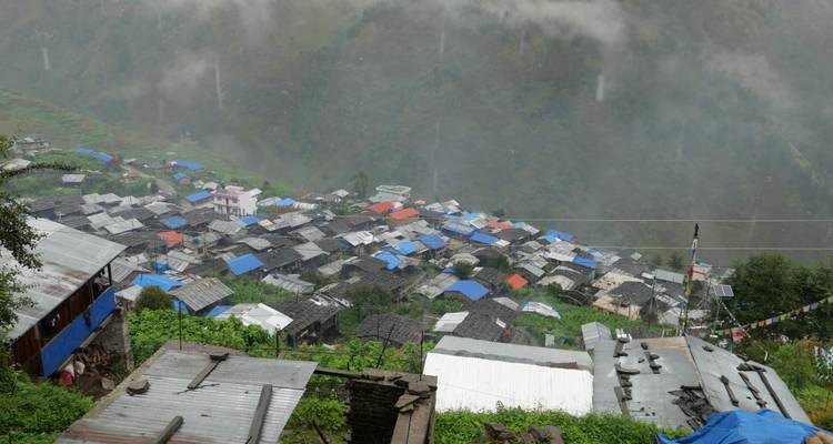Village de montagne sur une pente avec des toits gris et bleus aperçus à travers la brume et la pluie légère.