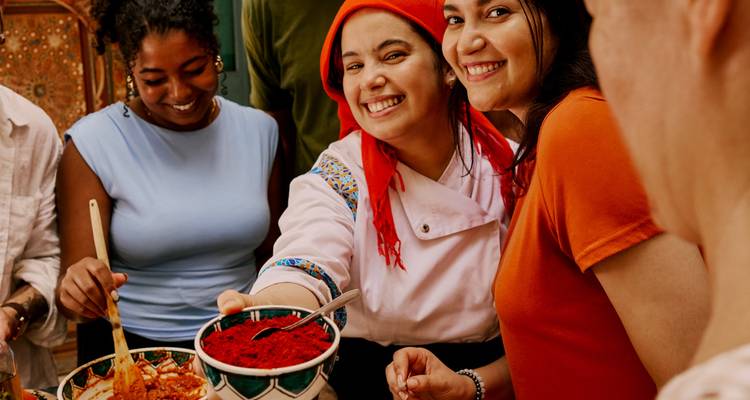 Grupo de personas con vestimenta tradicional marroquí, con una mujer local ofreciendo especias.