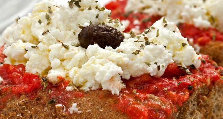 Gros plan sur un dakos grec traditionnel garni de tomate, fromage feta et une olive.